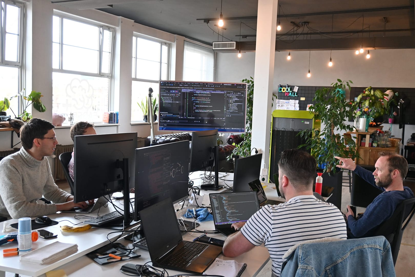 Een groep collega's, omringd door schermen, bespreken samen broncode.